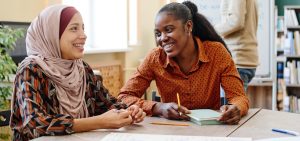 Young Black and Middle Eastern women having fun chatting about something during English lesson for immigrants