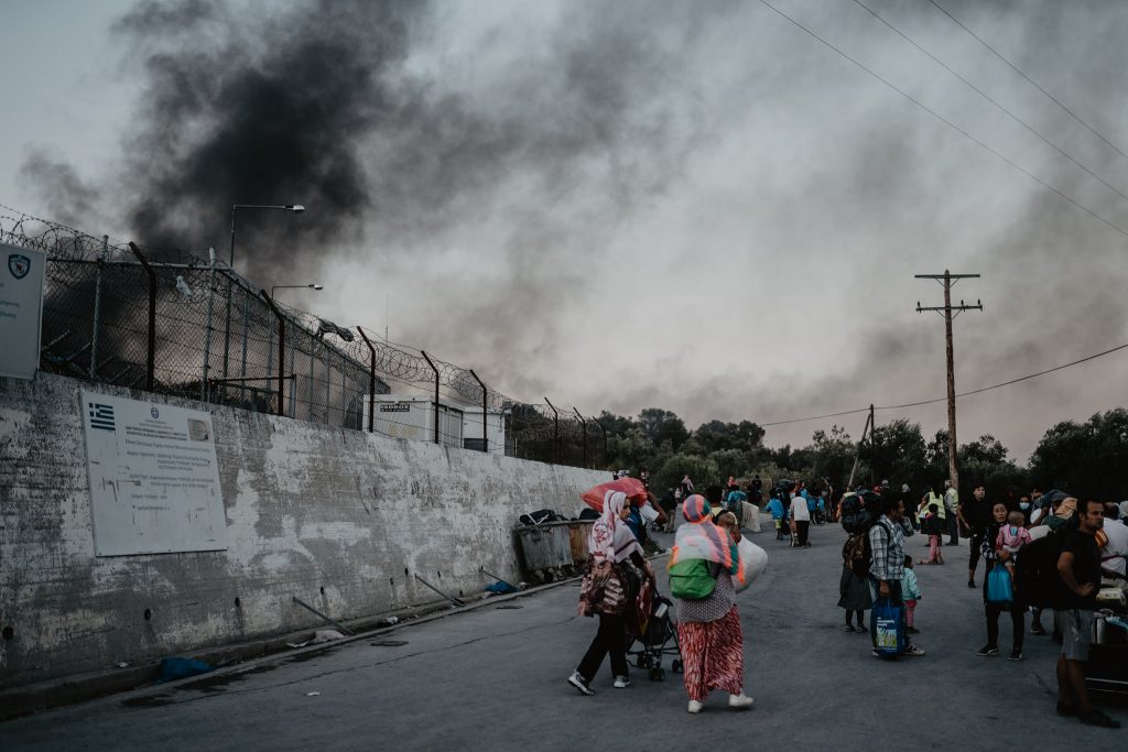 Black smoke over the walls of Camp Moria, parents and children evacuated outside.